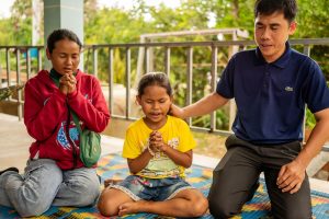 TOLA (CENTER) JOINS PASTOR KOSAL (RIGHT) IN PRAYER AT A COMMUNITY EVENT.